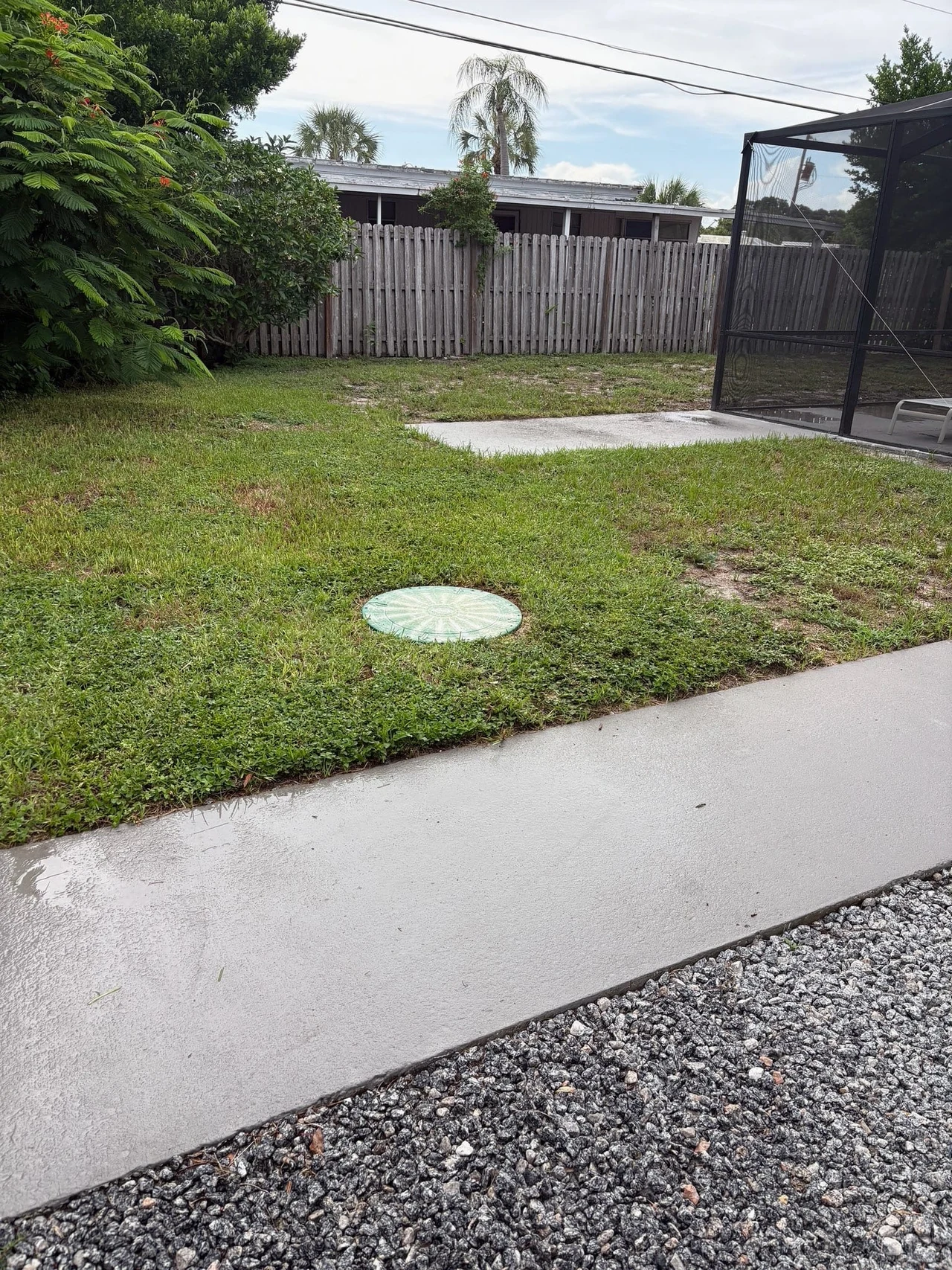 Closed green septic access lid in the lawn beside a screened patio